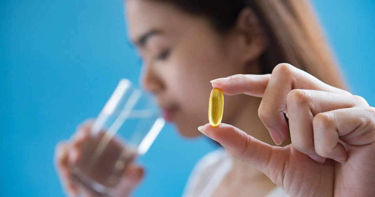 Woman holding a yellow supplement capsule with a glass of water.